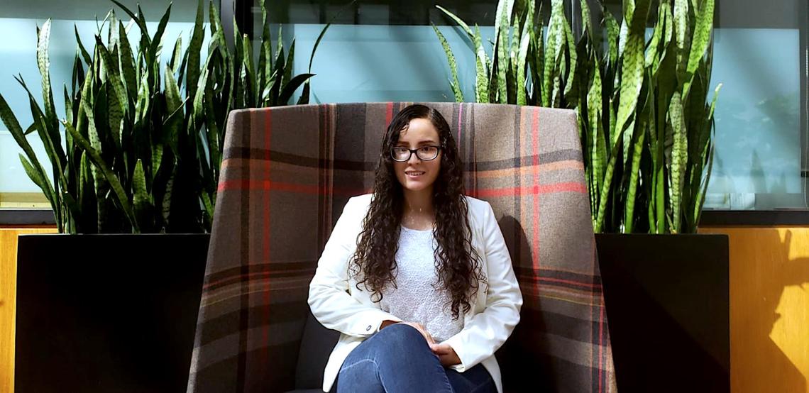 Student Valeria Marino sitting in a large chair with two large plants behind her