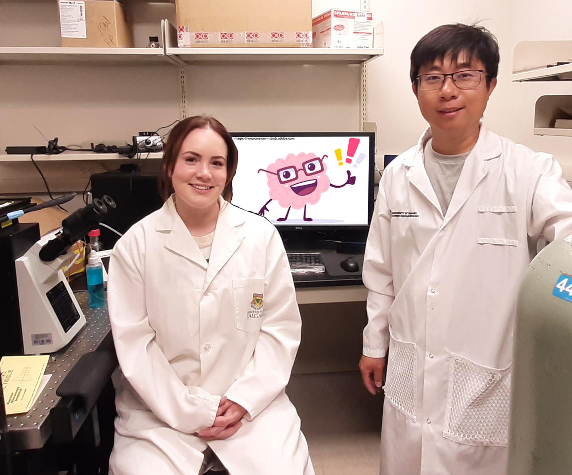 Two scientists wear white lab coats and stand in front of a monitor with a picture of a cartoon brain wearing glasses