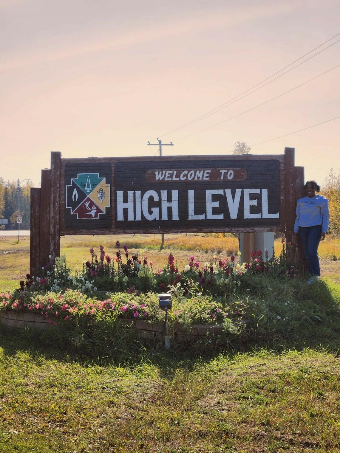 Tolu stands in front of "Welcome to High Level" sign