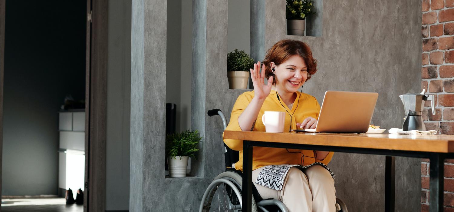 A woman in a wheelchair waving at computer screen