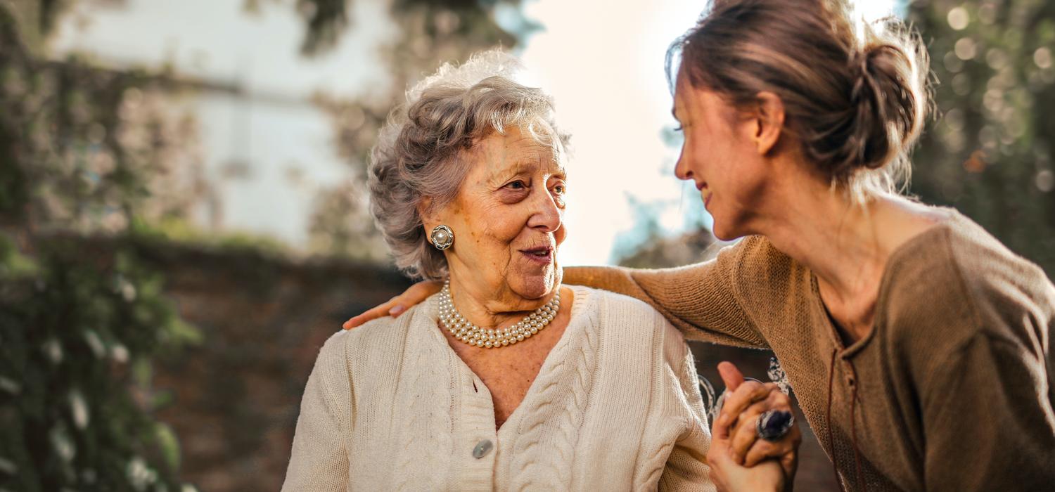A joyful adult daughter greets her happy surprised senior mother in a garden