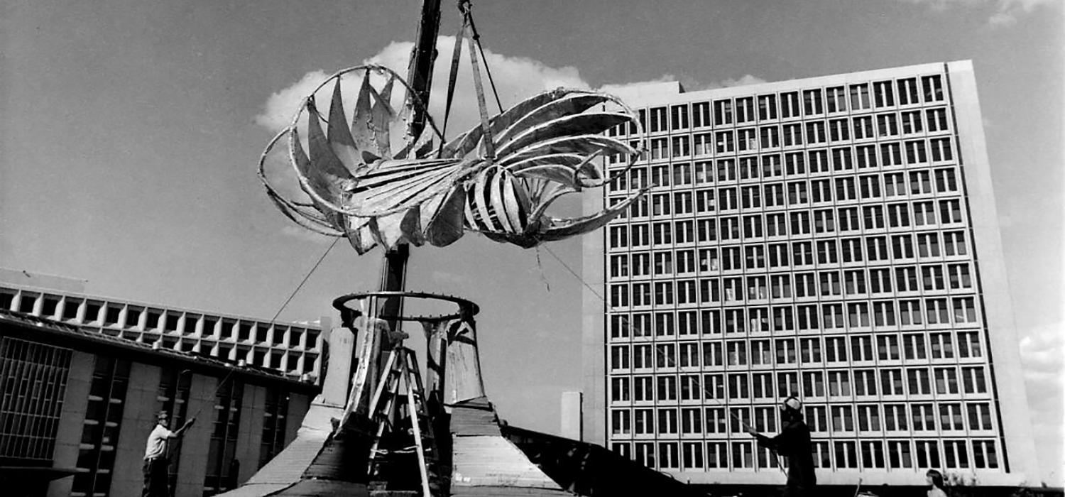 Image of a crane lowering the top of the Norris Sculpture (also known as The Prairie Chicken) onto the base