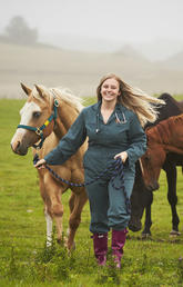 Woman leads horse in pasture