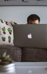 Person working behind computer on a brown couch