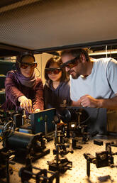 Three people in goggles work on a quantum machine